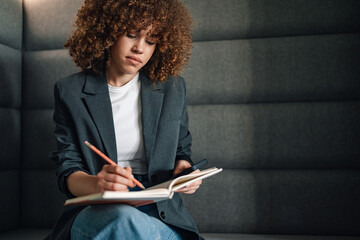 Focused businesswoman with textbook in her lap writing schedule at office