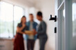 © Drazen - Close up of open door with real estate agent and buyers in background.