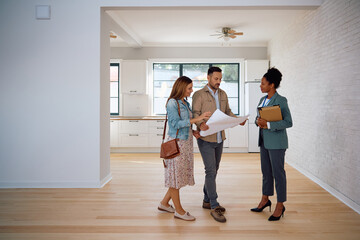 Wall Mural - Mid adult couple analyzing blueprints with real estate agent during open house day.