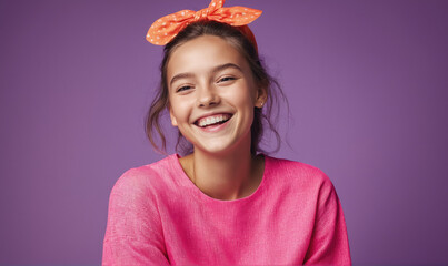 A young woman smiles brightly while wearing a pink sweater and a polka-dotted headband