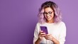 © Rstm - A young woman with purple hair smiles as she looks down at her phone. She is wearing a white shirt and is standing against a purple background.