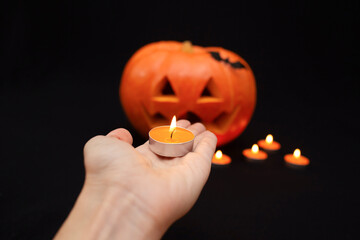 hand puts candles next to an orange Halloween pumpkin on a black background. dark background for halloween