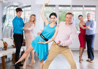 Cheerful men and women in festive clothes practicing tango dances in ballroom