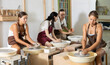 © JackF - Positive young lady wearing apron modeling clay dish from row material using pottery wheel in taller workroom