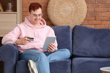 Sticker - Handsome young man with credit card and tablet computer sitting on sofa while shopping online