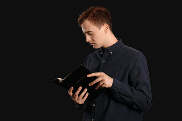 Poster - Young redhead man reading Bible on black background