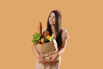 Young woman holding paper bag with fresh vegetables and fruits on brown background