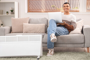 Sticker - Young man with laptop warming near radiator at home