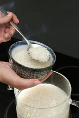 Wall Mural - Woman taking boiled rice from pot into bowl, closeup