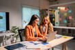 © Wasana - Two young businesswomen working late analyzing financial data on laptop in modern office