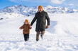 © alexkoral - Dad and son run along a snow-covered slope against the backdrop of a mountain landscape in winter.
