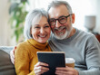 © payhip.com/YueAIArt - Happy Senior Couple Relaxing at Home with Tablet and Coffee, Smiling Mature old man and lady Enjoying a Cozy Morning Indoors Living Room Together with iPad Technology, elderly  woman grandpa grandma