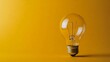 © Elmira - A bright lightbulb stands alone against a solid yellow backdrop, showcasing its clear glass and delicate filament, emphasizing its illuminating qualities and design