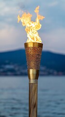 Poster - A burning torch with a wooden handle stands on a beach by the water.