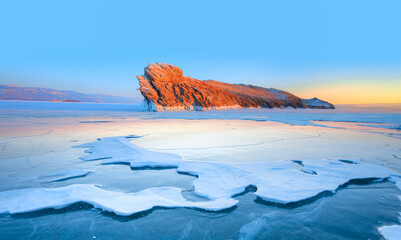 Wall Mural - A granite rock with steep slopes rises above a frozen lake with reflection on the ice at sunset -  Lake Baikal, Russia