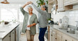 © peopleimages.com - Elderly couple, dancing and love in home, support and holding hands for laughing in kitchen. People, commitment and together for connection in relationship, bonding and romance or loyalty in marriage