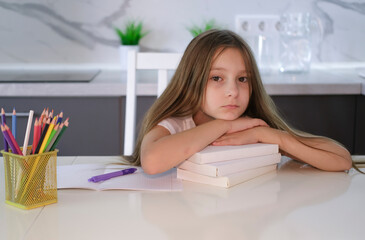 Wall Mural - Portrait of tired, sad girl falling asleep at table while doing her homework. Child concentrates and focuses on task for elementary school. Back to school. Homeschooling concept.