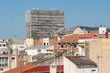 © yaqui_villegas - The image captures an urban landscape with various rooftops and a distinctive tall building in the center, showing a bustling city environment under a clear sky in Gracia Barcelona
