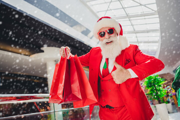 Poster - Photo of confident pretty santa claus wear dark glasses holding bargains showing thumb up indoors shopping center