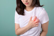 © Jirawatfoto - Chest pain or heart disease. Asian woman holding her chest pain from heart disease isolated on green background.