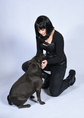 Poster - Full length portrait of beautiful black female model wearing sci fi futuristic dystopian leather bodysuit costume, with animal dog pet companion. sitting pose, isolated white studio background.