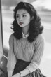 © siripimon2525 - A Japanese woman seated on a modern bench, her right hand resting on her knee while her left hand adjusts the sleeve of her sweater.
