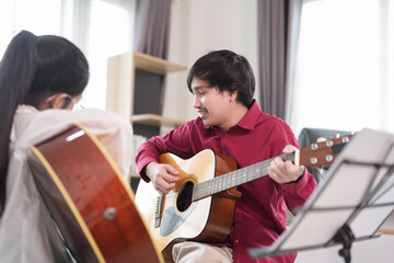 young asian male teaching a girl child playing guitar in the room,adult help kid to learn music,concept of music studying,music education,classical band