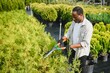 © Serhii - A african american young gardener cuts a tree with scissors. Gardening and tree shop concept