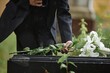 © Seventyfour - Close up on hand of unrecognizable senior woman placing white lilies on tombstone in memory of departed loved one while raindrops falling on grave at cemetery, copy space