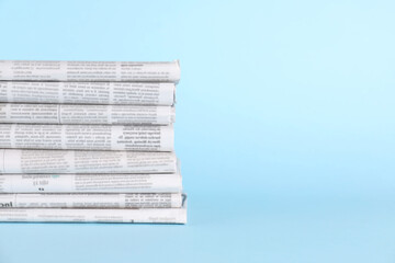 Canvas Print - Stack of newspapers in different languages on light blue background, space for text