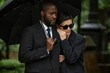 © Seventyfour - Medium shot of mourning multiethnic couple grieving at memorial ceremony. Senior woman clinging to Black mans shoulder hiding from rain under black umbrella at cemetery
