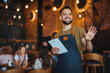 © Dragana Gordic - Smiling Waiter Greeting Customers in a Cozy Restaurant Setting