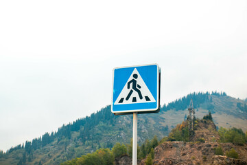 Pedestrian crossing road sign in the autumn mountains on the background. Kazakhstan, Almaty, Medeo. Hiking creative concept.