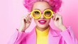 © angel_nt - A young woman with vibrant pink curly hair wears bold yellow sunglasses and a pink blazer. She smiles brightly against a lively pink backdrop, exuding fun and confidence