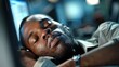 © angel_nt - A man is quietly sleeping at his desk in an office late at night, illuminated by the soft glow of computer screens, reflecting a sense of tranquility amid the work environment