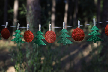 New Year's garland of green shiny fir trees and red shiny balls on clothespins in nature