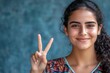 © mutter - Photograph of a lovely young lady dressed in a stylish colorful garment and isolated on a blue background with a V-sign