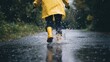 © Chatchanan - A person in a yellow raincoat and boots splashing through puddles on a deserted road