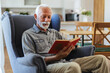 © Jelena Stanojkovic - Home, relax and senior man with a book, retirement and calm with a story in a living room. Old person, calm and pensioner in a lounge, novel or literature with a hobby, self help or reading on a sofa.