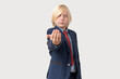 © somemeans - Portrait of a boy with blond hair wearing a blue suit and red tie making inviting gesture with his hand.