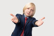 © somemeans - Portrait of young Caucasian boy with blond hair in suit and tie extends his arms for a hug and smiling at camera. Isolated on grey background.