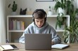 © Eva - Focused Young Student Engrossed in Online Learning at Home, Utilizing Laptop and Headphones.