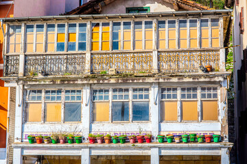 A view of a rustic balcony and facade typical of fishing districts in Spain. The building features faded paint, iron railings, and colorful potted plants, showcasing Spanish coastal architecture.