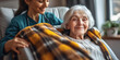 © IndigoElf - The nurse covers with a warm plaid a smiling old lady grandmother sitting in a chair. Home health care