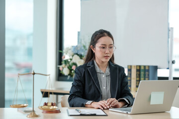 A woman in a business suit is sitting at a desk with a laptop