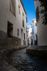 A small water stream flowing through a narrow alley of white buildings under a bright blue sky, Alpujarras, granada, andalucia, espa a