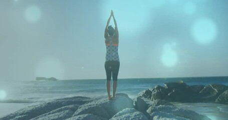 Wall Mural - animation of light spots over biracial woman practicing yoga at beach