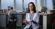 © Framestock - Female young scientist in lab coat talks to the camera and gives interview for popular science film while sitting in archaeological scientific lab. Male colleague works in the background. Static Shot.