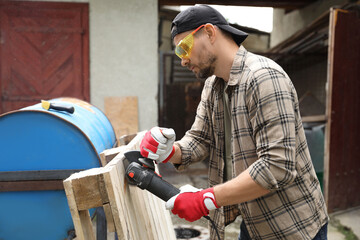 Canvas Print - Man grinding wooden planks with angle grinder outdoors