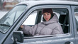 © July P - Woman wearing a maroon beanie and gray jacket, sitting in a car covered in snow. Outdoor winter scene, concept of traveling in winter weather.